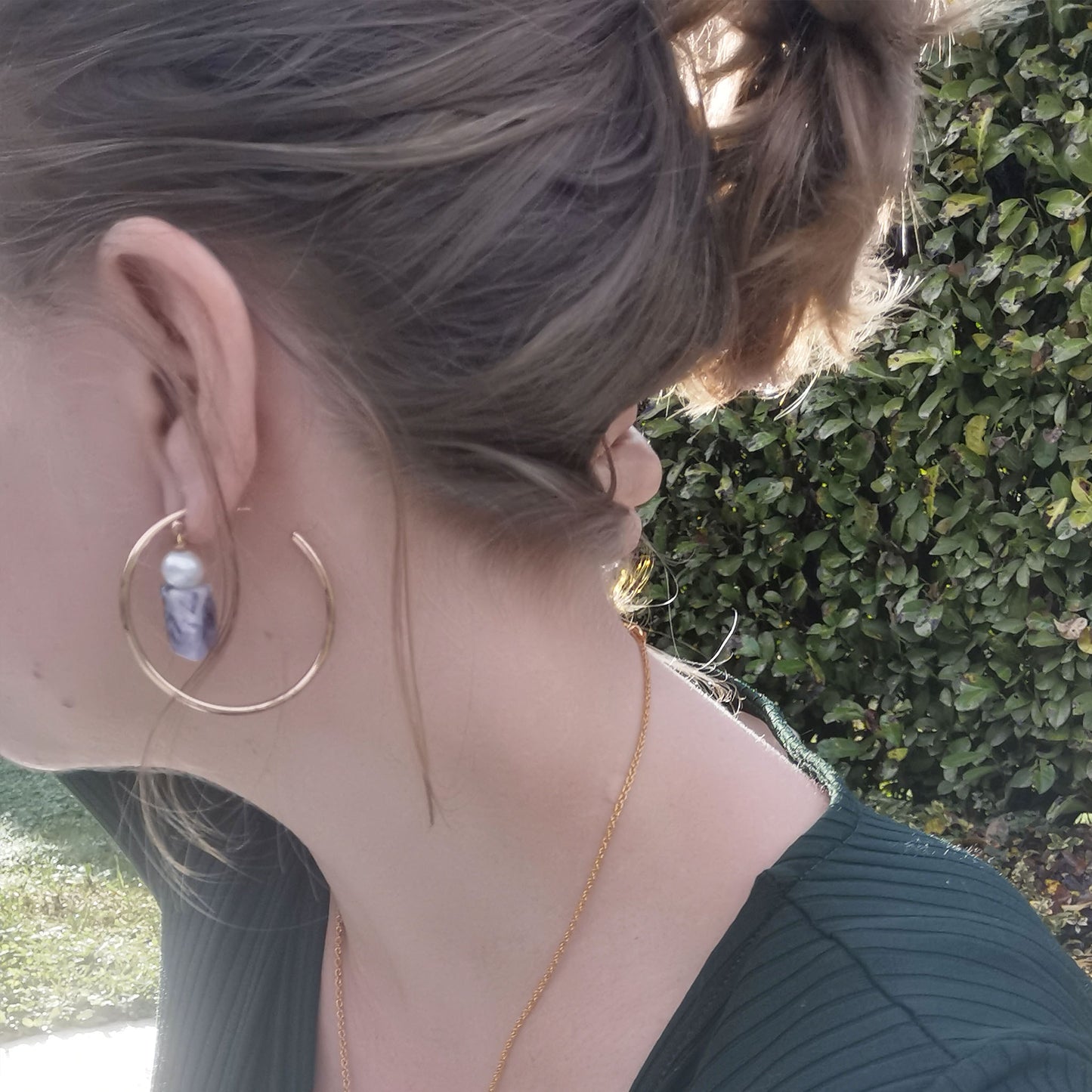 Purple pearl hoop worn with green top and foliage in background