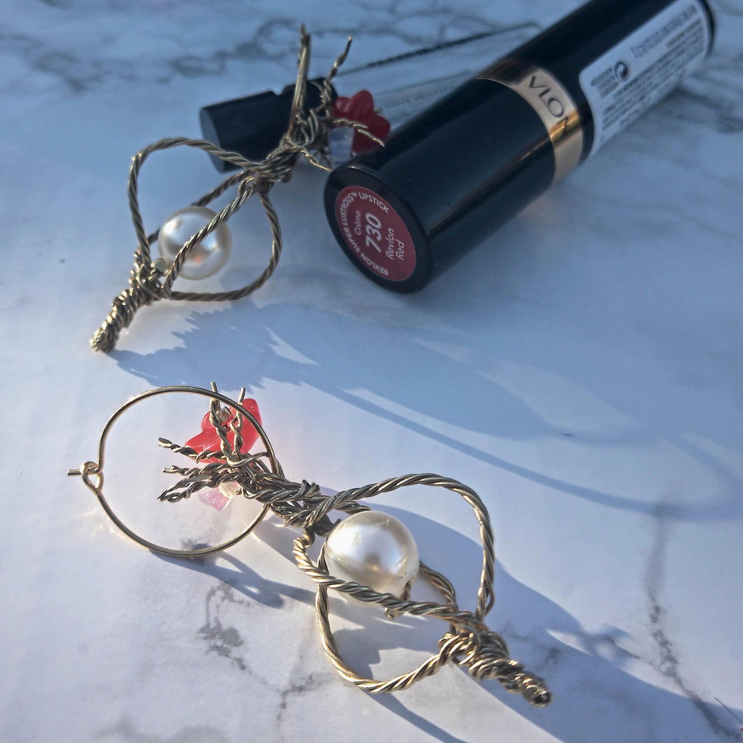 Twisted wire earrings with pearl and red bead deatails. Lifestyle shot with lipstick and perfume. 