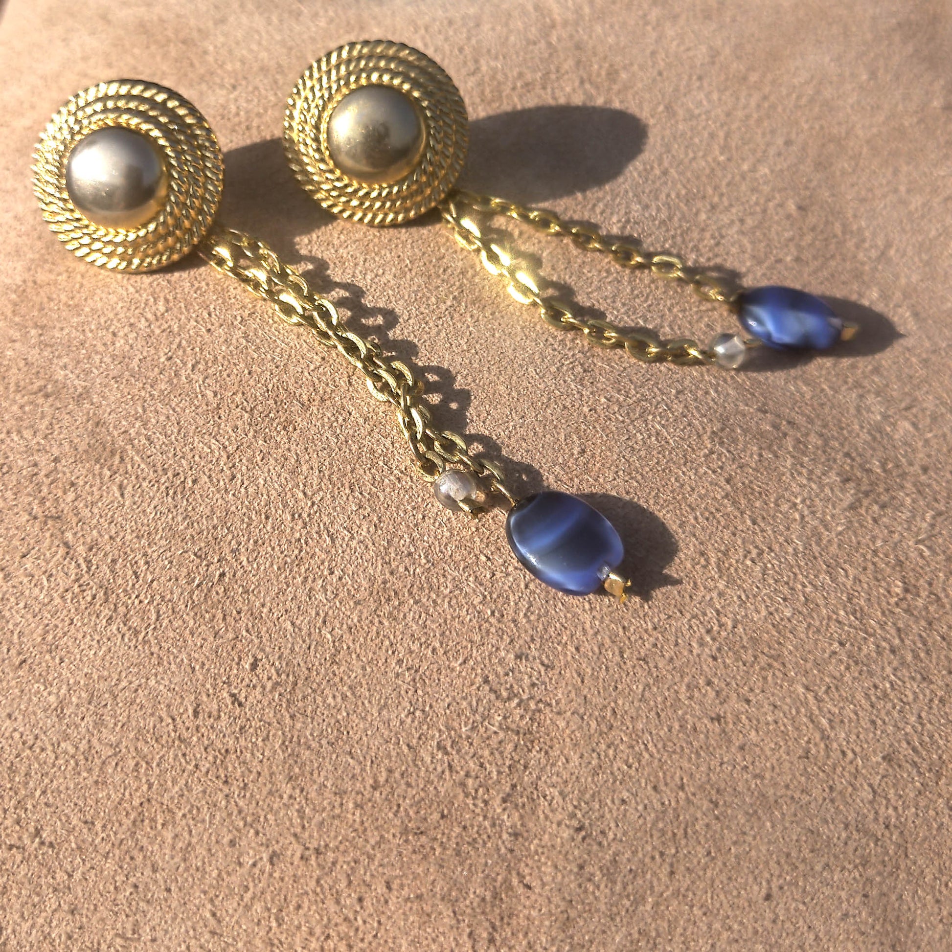 Textured stud with cable chain dangle and blue and see-through beads on suede background 