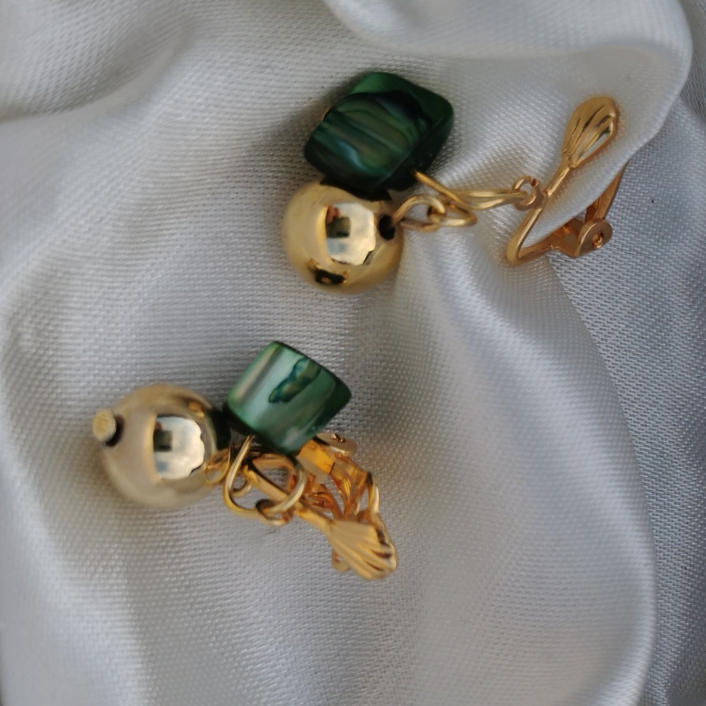 Green shell and bell clip on earrings photographed on silk 