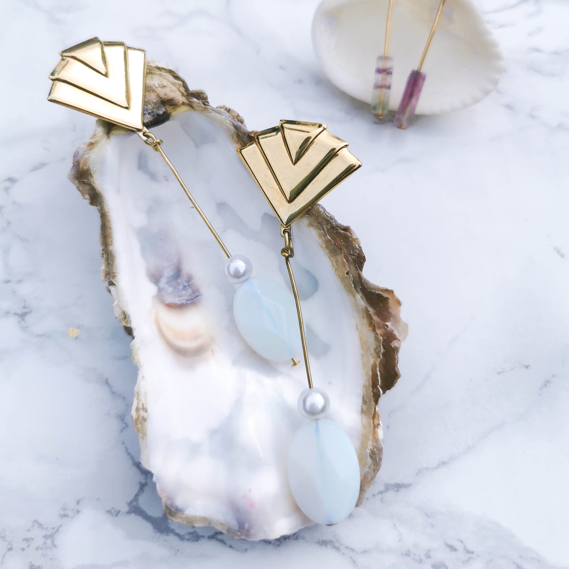 Fan studdded earring with opal and boehem pearl drop on pin posed on oyster shell