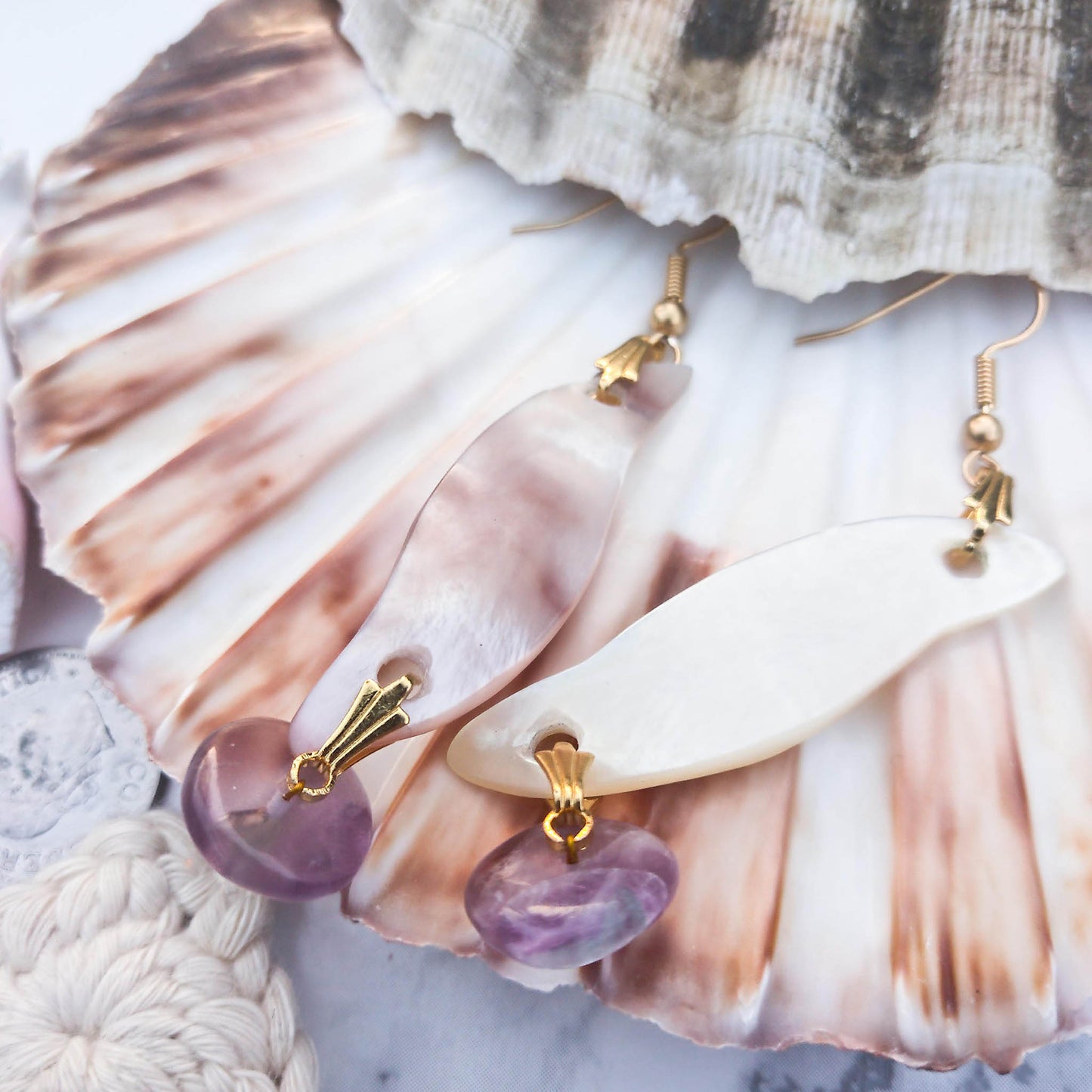 Earrings with curved mother od pearl, gold a and fluorite details lying on a shell